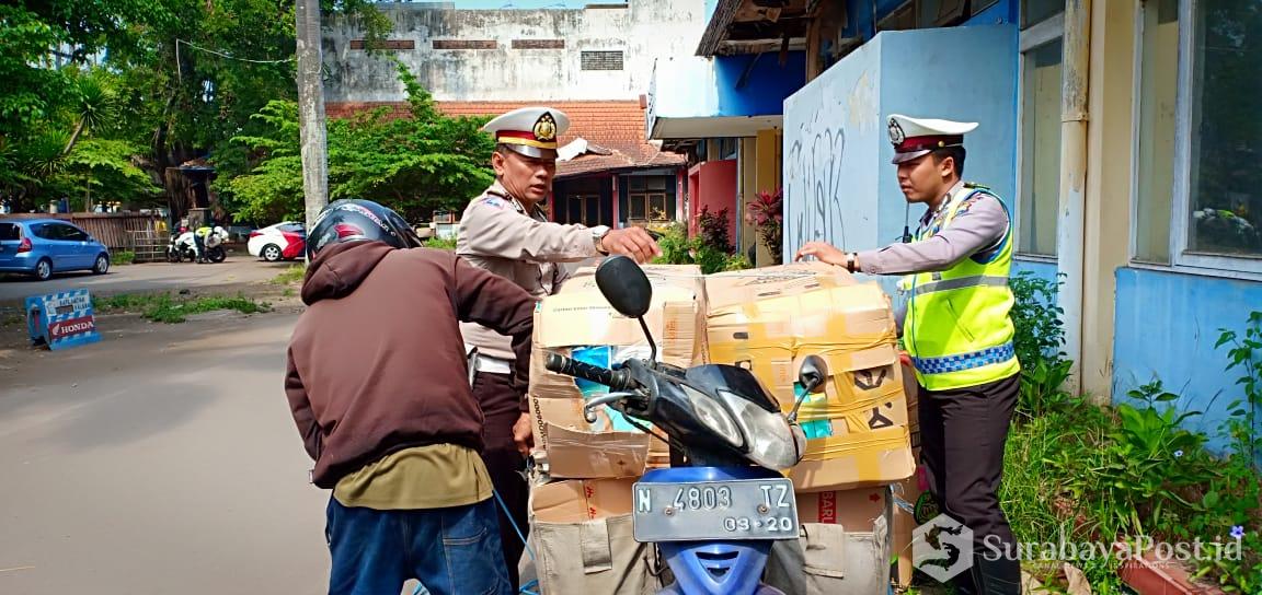 Kanit Laka Polres Malang Kota, Ipda Deddy Catur (kiri) turut membantu menurunkan barang bawaan salah satu pengendara yang terjaring razia