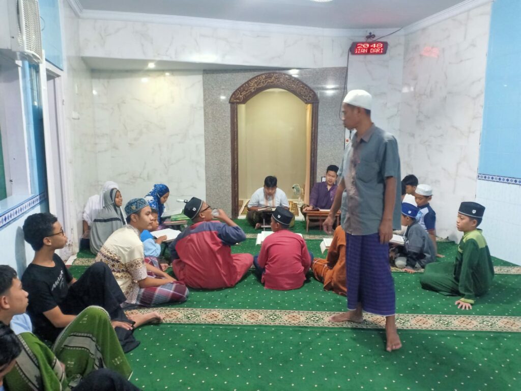 Ustad Suyanto (berdiri) memantau anak didiknya dari TPQ Az Zahro' dalam kegiatan Tadarus Alquran di Masjid Babul Hidayah