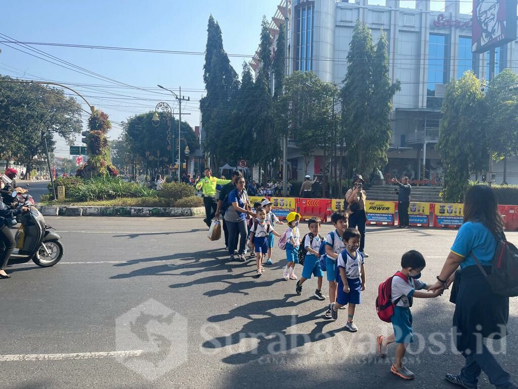 SIMPATIK: Anggota Satlantas Polresta Malang Kota membantu siswa TK beserta para guru menyeberang jalan (ist)