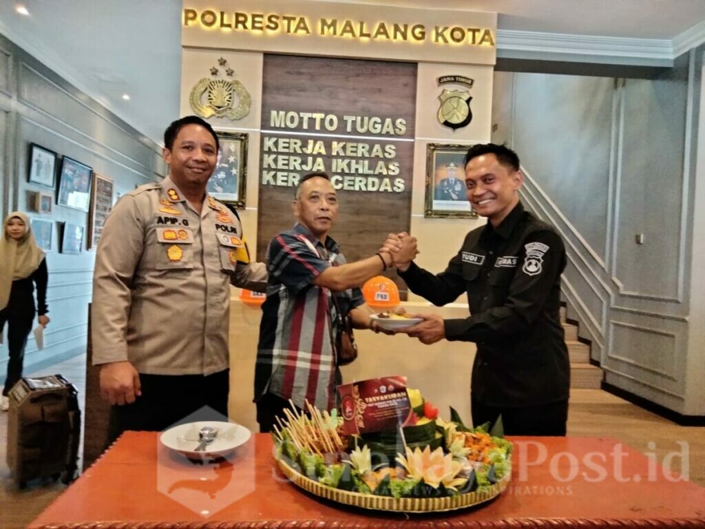 Kasi Humas Polresta Malang Kota, Ipda Yudi Rusdianto memberikan potongan nasi tumpeng kepada Rokim Alfarizi, salah satu wartawan senior mitra Polresta Malang Kota