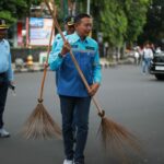 Wali Kota Malang, Dr. Ir. Wahyu Hidayat, M.M., turut turun tangan membersihkan trotoar. Nampak ia memegang sikat dan mulai menggosok trotoar yang sebelumnya terlihat kusam dan berdebu. (Sumber Prokompim).