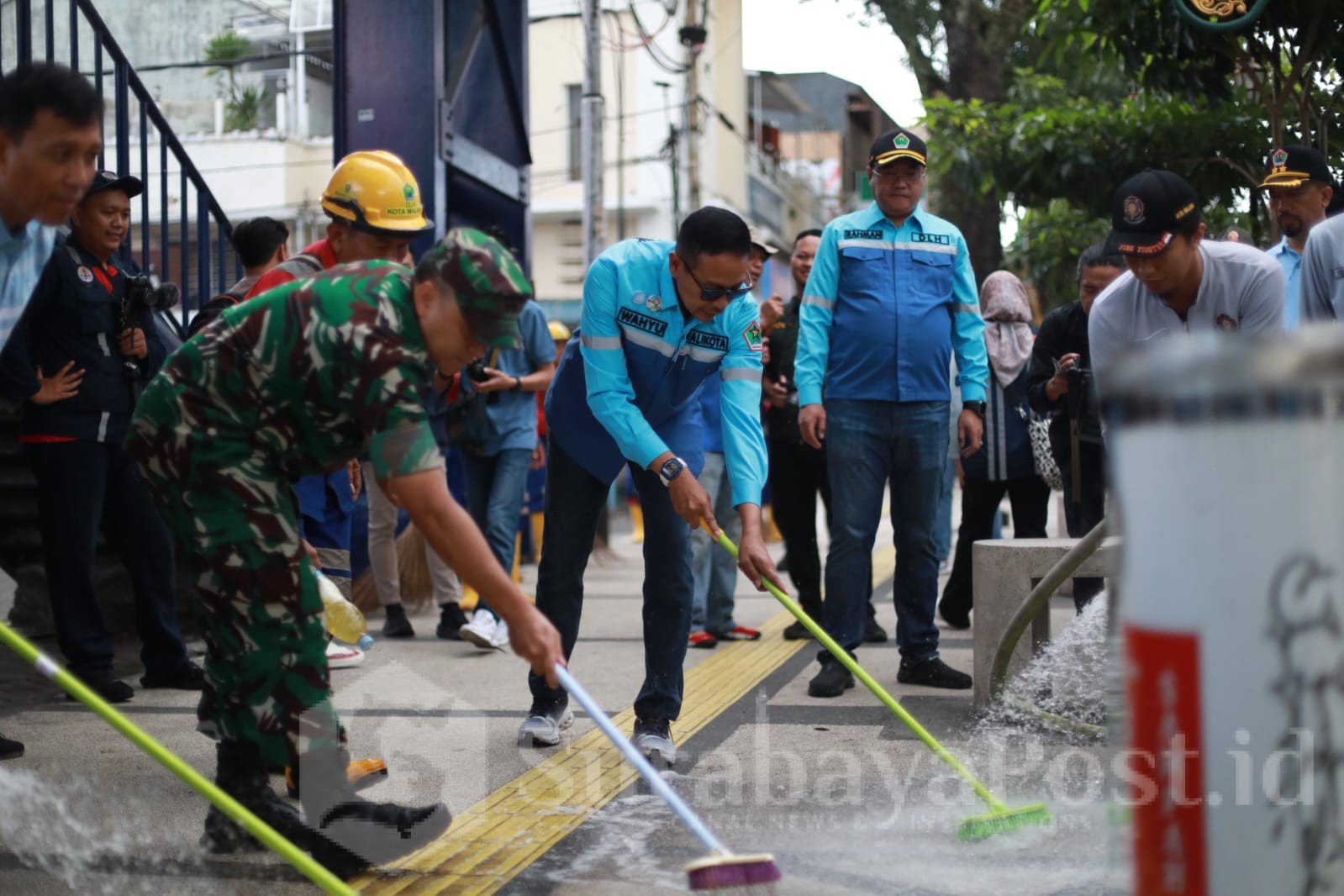 Wali Kota Malang, Dr. Ir. Wahyu Hidayat, M.M., turut turun tangan membersihkan trotoar. Nampak ia memegang sikat dan mulai menggosok trotoar yang sebelumnya terlihat kusam dan berdebu. (Sumber Prokompim).