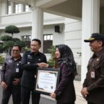 Wali Kota Malang, Dr. Ir. Wahyu Hidayat, M.M., menyerahkan piagam penghargaan WBBM tersebut kepada Kepala Dispendukcapil Kota Malang, Ir. Dahliana Lusi Ratnasari, M.M. (Sumber Prokompim).